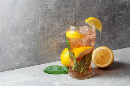 Photo for Iced tea with ice, mint, and lemon. A cold refreshing drink with ingredients on a grey background. Copy space. - Royalty Free Image