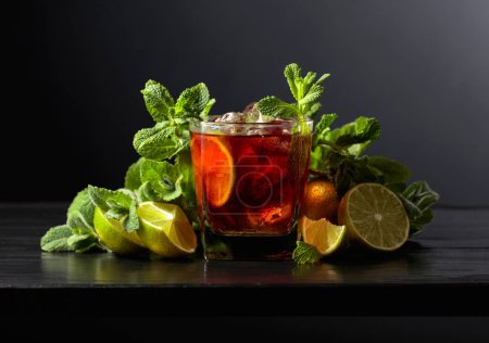 Téléchargez les photos : Cocktail Cuba Libre au rhum, cola, menthe et citron vert sur une table en bois noir. - en image libre de droit