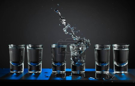 Téléchargez les photos : Des verres alcoolisés de vodka ou de boisson forte dans de petits verres. Un morceau de glace tombe dans un verre, créant un éclaboussure. Espace de copie. - en image libre de droit