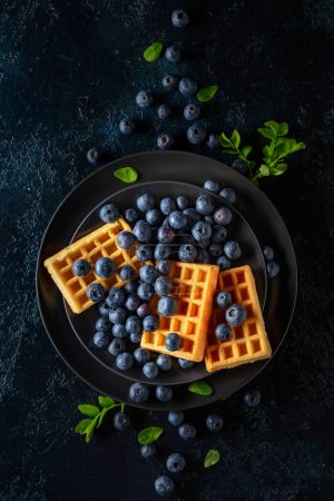 Photo for Belgian waffles with blueberries on a black plate. Top view. - Royalty Free Image