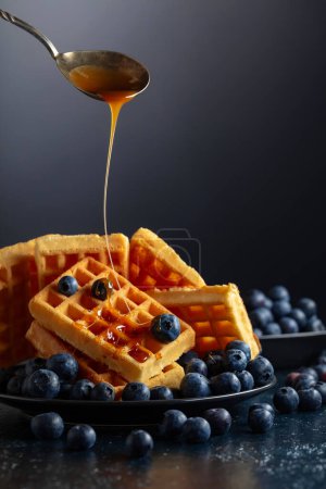 Photo for Belgian waffles with fresh blueberries and caramel sauce on a black plate. - Royalty Free Image