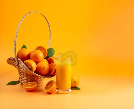 Téléchargez les photos : Verre de jus d'orange avec des fruits frais dans le panier sur un fond d'orange. Espace de copie. - en image libre de droit