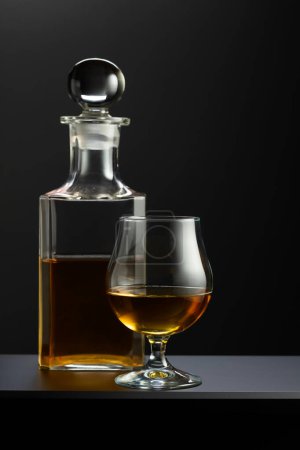 Foto de Decantador viejo y vaso con whisky, coñac o brandy sobre fondo negro. - Imagen libre de derechos