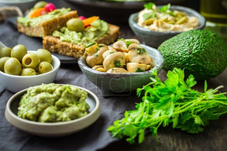 Foto de Snacks veganos de comida cruda con verduras frescas jugosas, salsa de aguacate, humus y champiñones marinados - Imagen libre de derechos