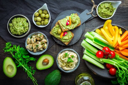 Photo for Vegan raw food snacks with fresh juicy vegetables, avocado dip, humus and marinated mushrooms - Royalty Free Image