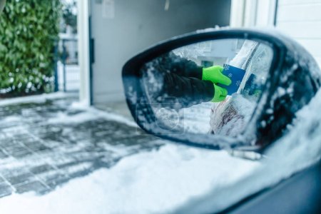Foto de Teenager  cleans car after a snowfall, removing snow and scraping ice - Imagen libre de derechos