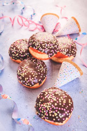 Foto de Chocolate Berliner pastry for carnival and party. German Krapfen or donuts with streamers and confetti.  Colorful carnival or birthday image - Imagen libre de derechos