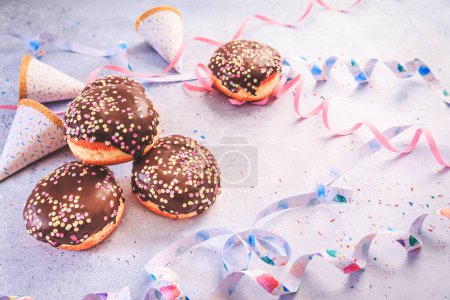 Téléchargez les photos : Chocolate Berliner pastry for carnival and party. German Krapfen or donuts with streamers and confetti.  Colorful carnival or birthday image - en image libre de droit