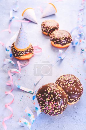 Téléchargez les photos : Chocolate Berliner pastry for carnival and party. German Krapfen or donuts with streamers and confetti.  Colorful carnival or birthday image - en image libre de droit
