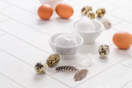 Foto de Huevos diferentes con plumas para Pascua sobre fondo blanco - Imagen libre de derechos
