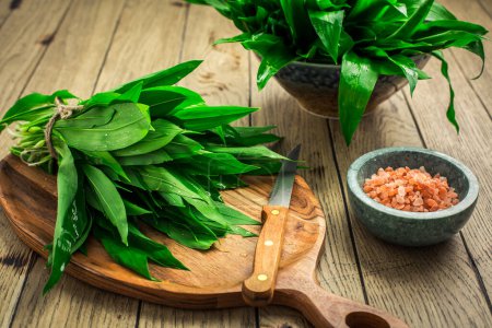 Photo for Fresh wild leek leaves on a wooden board. Leaves of fresh ramson with pink Himalayan salt. - Royalty Free Image