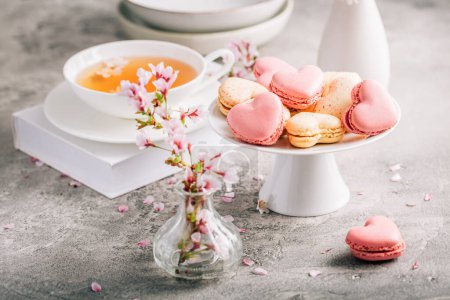 Photo for Macarons or French macaroons in heart shapes with tea with cherry blossom petals for Mothers Day - Royalty Free Image