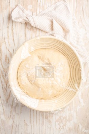 Photo for Raw yeast dough resting and rising in a special basket on kitchen table - Royalty Free Image