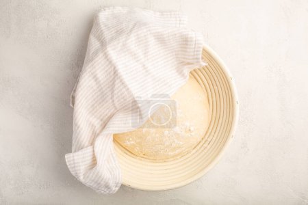 Téléchargez les photos : Pâte à levure crue reposant et se levant dans un panier spécial sur la table de cuisine - en image libre de droit
