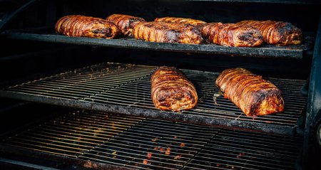 Photo for Large barbecue smoker grill at the park. Meat and bacon prepared in barbecue smoker. - Royalty Free Image