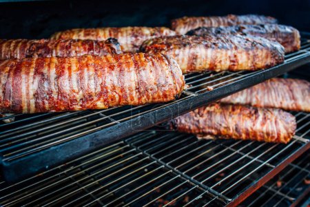Photo for Large barbecue smoker grill at the park. Meat and bacon prepared in barbecue smoker. - Royalty Free Image