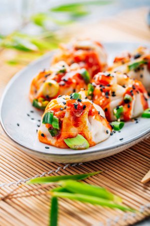 Téléchargez les photos : Boulettes cuites à la vapeur Dim Sum avec sauce Sriracha piquante et oignons verts et graines de sésame. - en image libre de droit