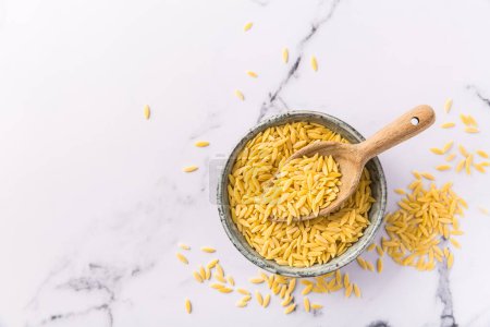 Raw orzo pasta (risoni) in bowl with wooden spoon