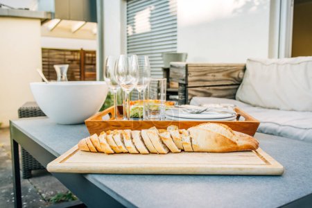 Téléchargez les photos : Baguette fraîchement cuite avec collation saine et verres sur terrasse ou patio - en image libre de droit