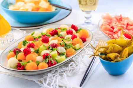 Foto de Comida ligera de verano. Ensalada de pepino y melón con frambuesas y jamón y pimientos picantes en escabeche - Imagen libre de derechos
