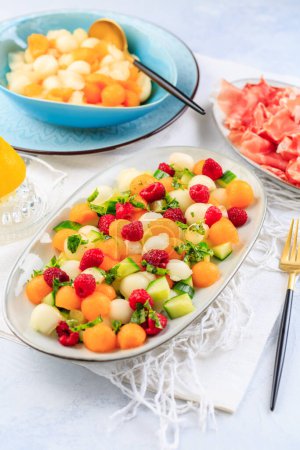 Photo for Summer light food. Cucumber and melon salad  with raspberries and Prosciutto and pickled hot peppers - Royalty Free Image