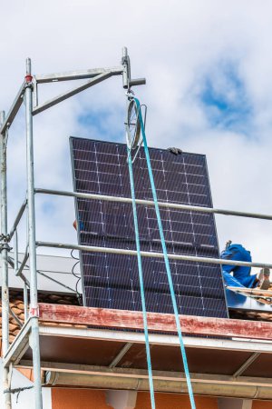 Téléchargez les photos : Levage de panneaux solaires à l'aide d'une poulie. Installation de panneaux solaires sur un toit. Panneaux solaires sur le toit. Travailleurs installant des cellules solaires. - en image libre de droit