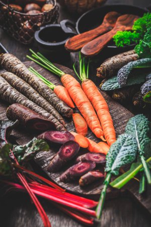 Foto de Verduras orgánicas crudas de invierno en la mesa de la cocina con zanahorias, castañas, acelgas, col rizada - Imagen libre de derechos