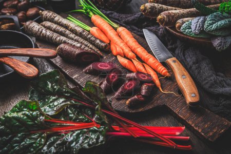 Foto de Verduras orgánicas crudas de invierno en la mesa de la cocina con zanahorias, castañas, acelgas, col rizada - Imagen libre de derechos
