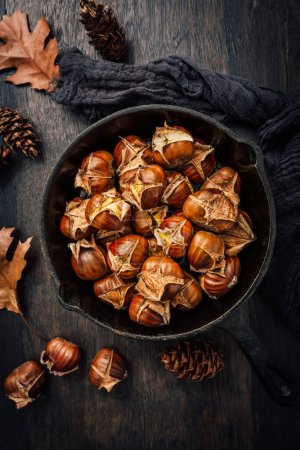 Téléchargez les photos : Marrons rôtis dans une casserole en fer sur une vieille table de cuisine - en image libre de droit