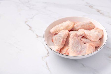 Photo for Raw chicken wings in white bowl, prepared for cooking on marble background - Royalty Free Image