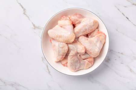 Photo for Raw chicken wings in white bowl, prepared for cooking on marble background - Royalty Free Image
