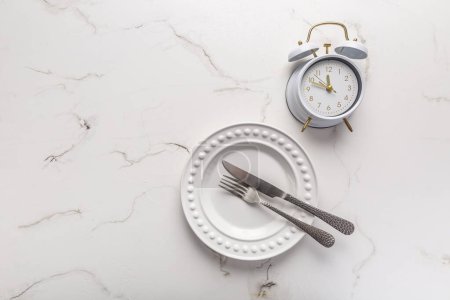 Téléchargez les photos : Concept of intermittent fasting, empty plate with clock on white - en image libre de droit