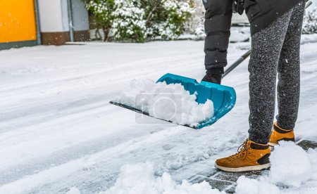 Téléchargez les photos : Nettoyage de la neige de la rue en hiver avec une pelle après une tempête de neige. Nettoyage du trottoir de la neige un jour d'hiver. - en image libre de droit