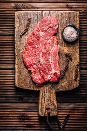 Téléchargez les photos : Steak de boeuf cru Chuck eye assaisonné de sel et de poivre sur planche à découper en bois - en image libre de droit