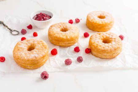 Foto de Cronuts - deliciosa fusión de croissant y donut con mermelada de frambuesa. Pastelería a medio donut y medio croissant - Imagen libre de derechos