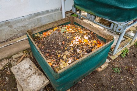 Compost bin with food scraps, grass cuttings, weeds and organic leftovers as natural fertilizer