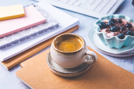 Téléchargez les photos : Pause café dans un bureau, tasse de café avec du yaourt sain dans un bureau. Lieu de travail dans un café ou un bureau à domicile - en image libre de droit