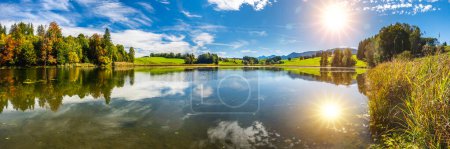 Téléchargez les photos : Vue panoramique sur le lac avec reflet symétrique du soleil sur le ciel - en image libre de droit