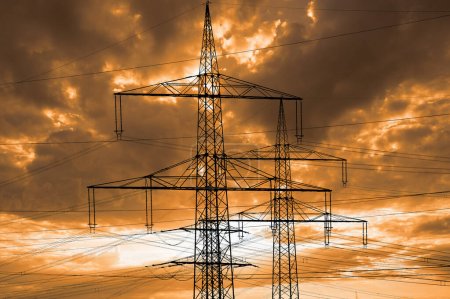 high voltage pylons for electricity and power against sky with dramatic clouds