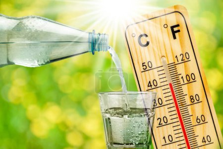 Téléchargez les photos : Thermomètre montre une température élevée en été chaleur et bouteille avec de l'eau avec verre à boire - en image libre de droit