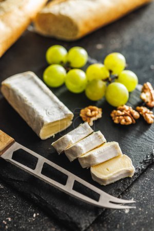 Gros plan détaillé d'un fromage Brie coupé accompagné de raisins croustillants sur une surface d'ardoise noire, mettant en valeur la texture et la forme