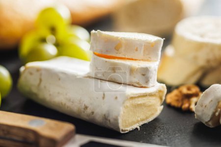 Gros plan détaillé d'un fromage Brie coupé accompagné de raisins croustillants sur une surface d'ardoise noire, mettant en valeur la texture et la forme