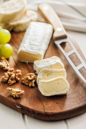 Artisan Brie cheese sliced on a round wooden cutting board, served with grapes and walnuts, ideal image for Gourmet cheese concepts