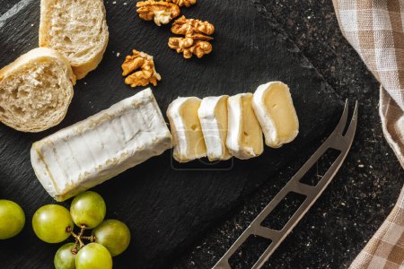 Primer plano detallado de un queso Brie cortado acompañado de uvas crujientes sobre una superficie de pizarra negra, destacando la textura y la forma