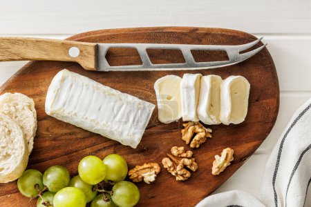 Artisan Brie cheese sliced on a round wooden cutting board, served with grapes and walnuts, ideal image for Gourmet cheese concepts