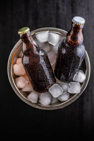 A metal bucket is filled with ice, and two glass bottles of beer are placed inside it, chilling.