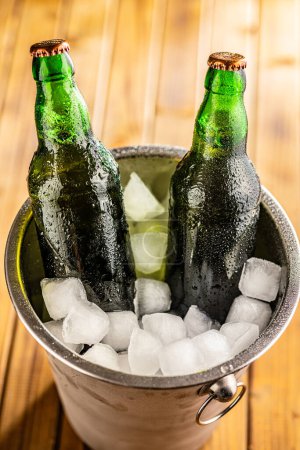 Ein Metalleimer ist mit Eis gefüllt, und zwei Glasflaschen Bier sind darin platziert, kühl.