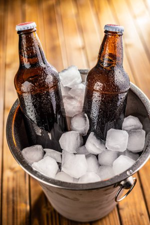 A metal bucket is filled with ice, and two glass bottles of beer are placed inside it, chilling.
