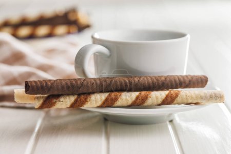 Assorted Chocolate and Vanilla Cream Filled Wafer rolls and coffee cup on a white table.