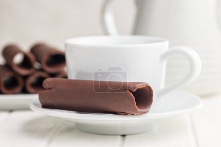 Ein Nahaufnahme-Foto von mit Schokolade überzogenen Oblatenrollen, die auf einem weißen Teller und einer Kaffeetasse gestapelt sind.